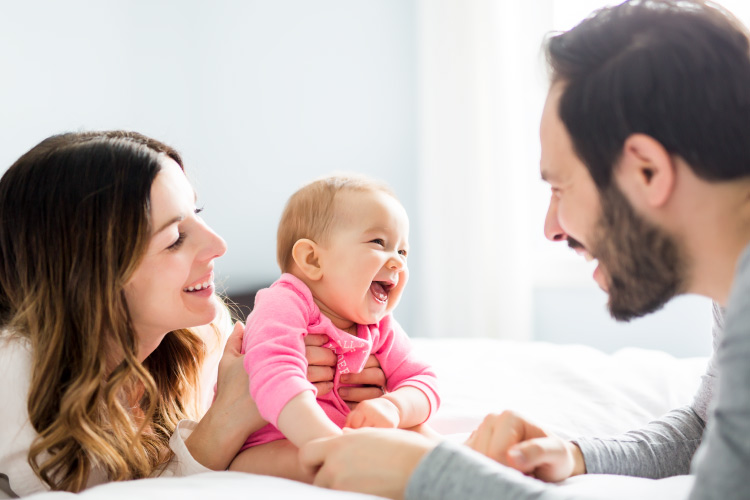 Brunette mom and dad smile happily at their baby girl getting her first baby teeth