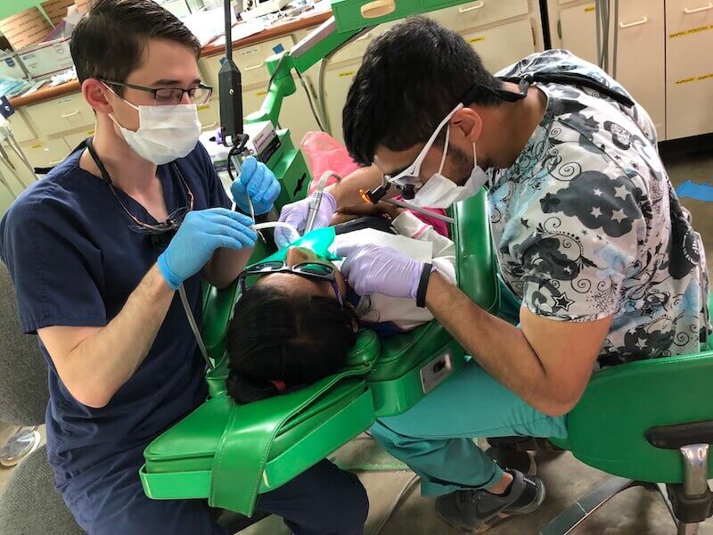 Dr. Patrick works on the teeth of a child in Guatemala on a green dental chair with an assistant