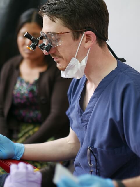 Dr. Patrick with magnifying lenses on his eyes while wearing blue scrubs in Guatemala