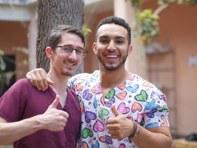 Dr. Patrick in maroon scrubs giving a thumbs up