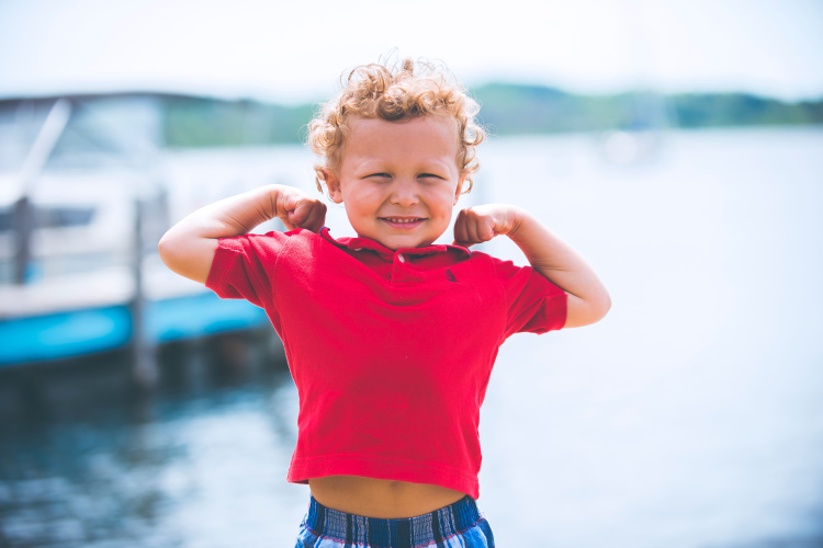 Young boy wearing a red polo flexes his arms saying kids are strong and able to combat their dental fear