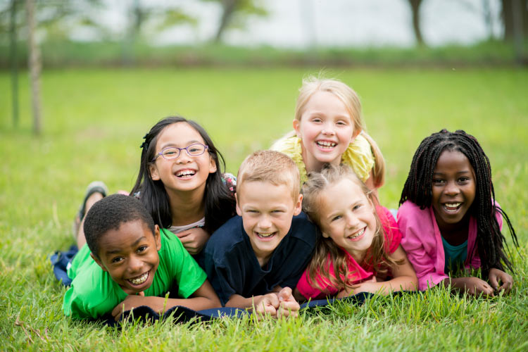 Group of multiracial kids smile without cavities in the grass by Storybook Smiles in Tyler, TX