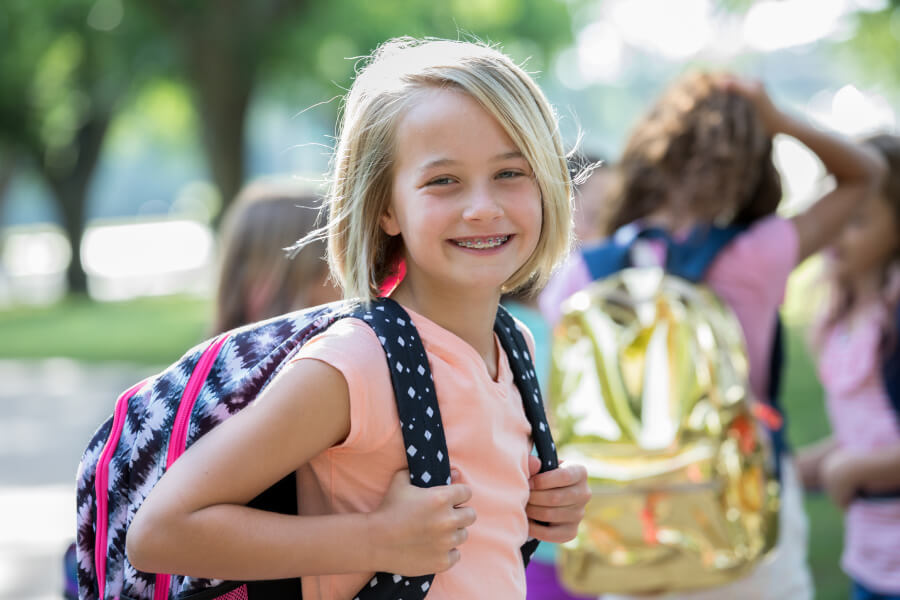 Blonde girl wears braces as she carries her backpack into school