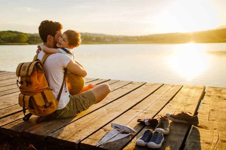 Dad embraces his son with special needs while sitting on a wooden dock by a lake in Tyler, TX