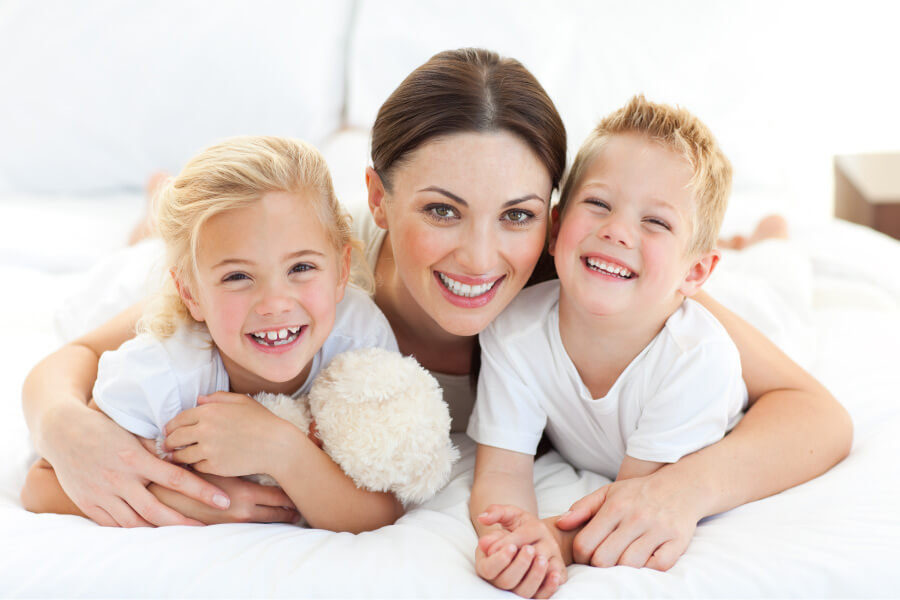 Brunette mom smiles with her two blonde children, one with crooked teeth that need braces