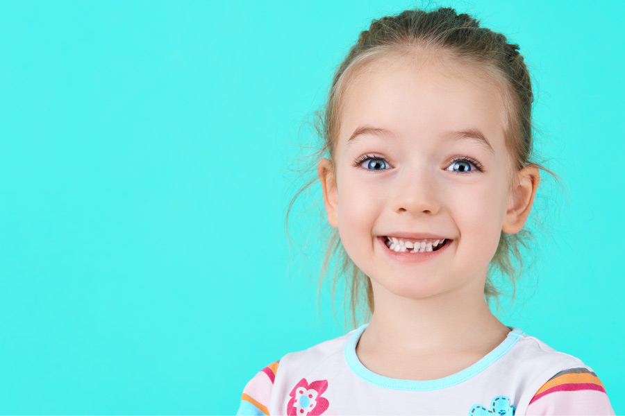 A young girl smiles with a missing baby tooth after it fell out to make way for her permanent tooth