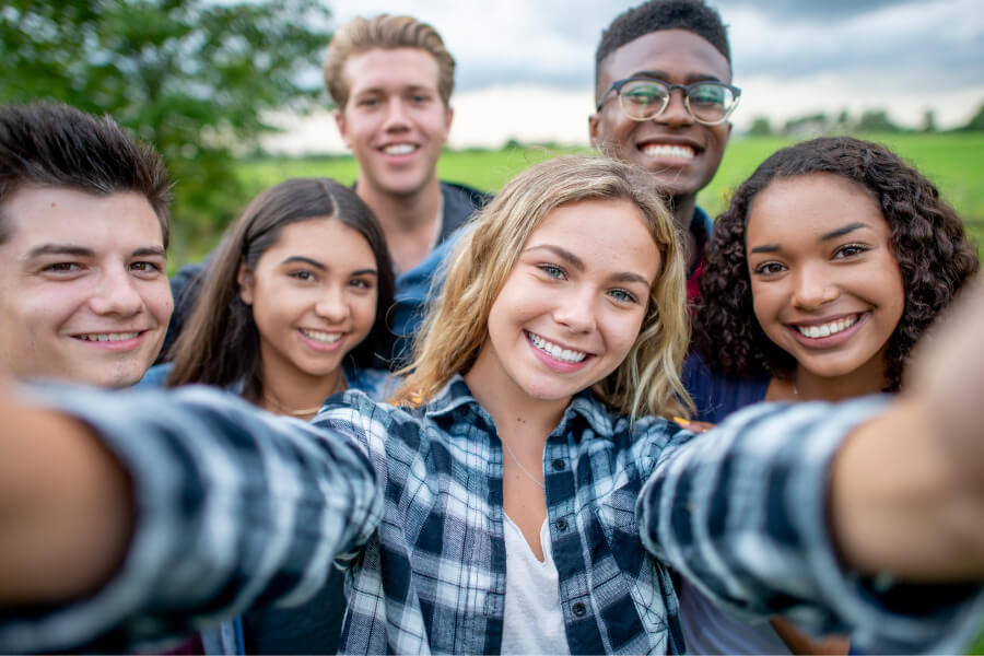 A diverse group of teenagers smile as they take a group selfie outside after teeth whitening for teens in Tyler, TX