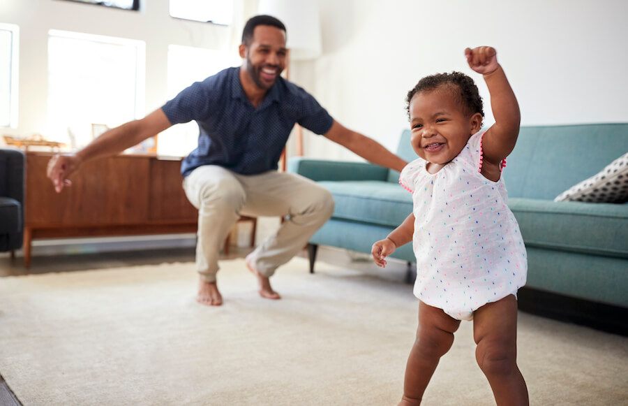 Black one year old girl dances in the family room with her dad before her first dental visit