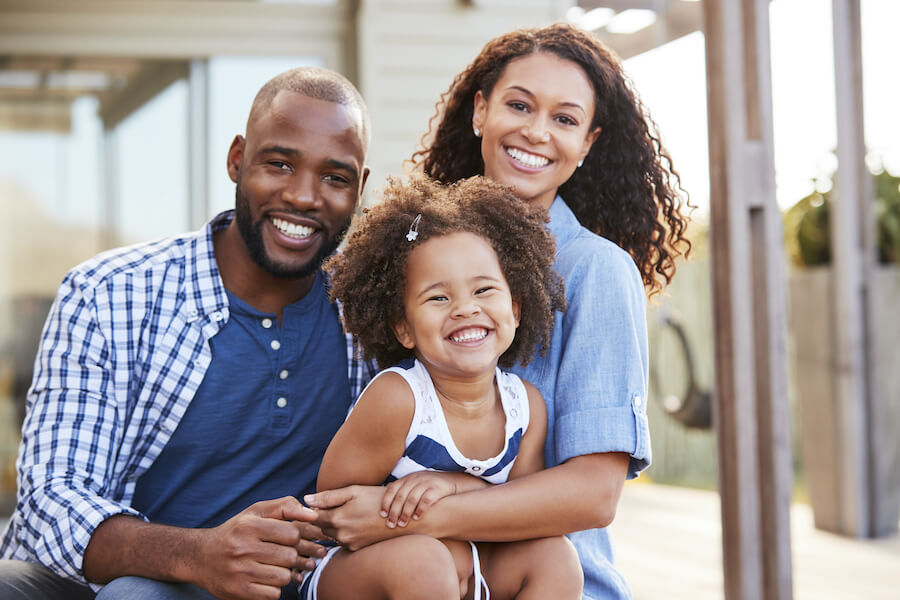 A Black mom and dad smile while hugging their young daughter