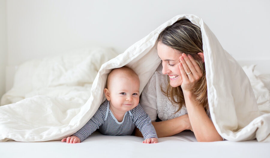 A mom gazes lovingly at her smiling, bald little baby during tummy time