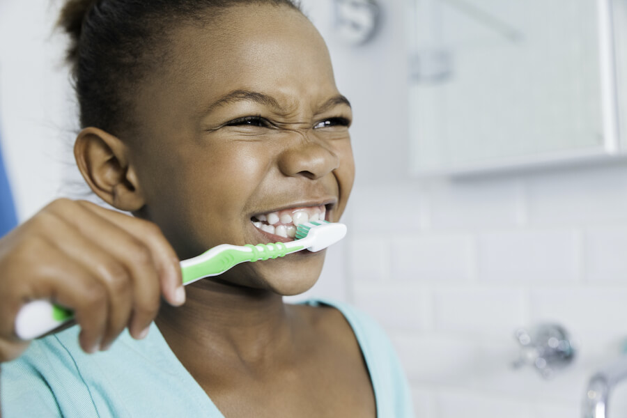 Closeup of a young Black girl smiling while brushing her teeth