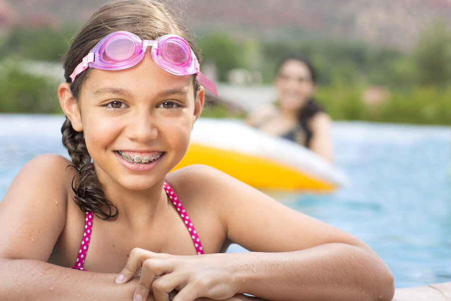 pre-orthodontic evaluation, photo of a smiling, young Hispanic girl with braces in a swimsuit. 