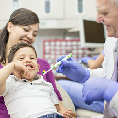 dentist showing young boy how to brush his teeth