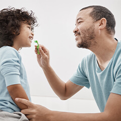 father showing his son how to brush his teeth
